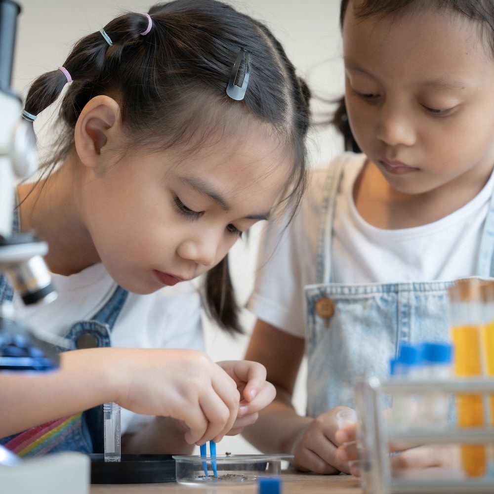 Two children use science equipment and petri dishes.