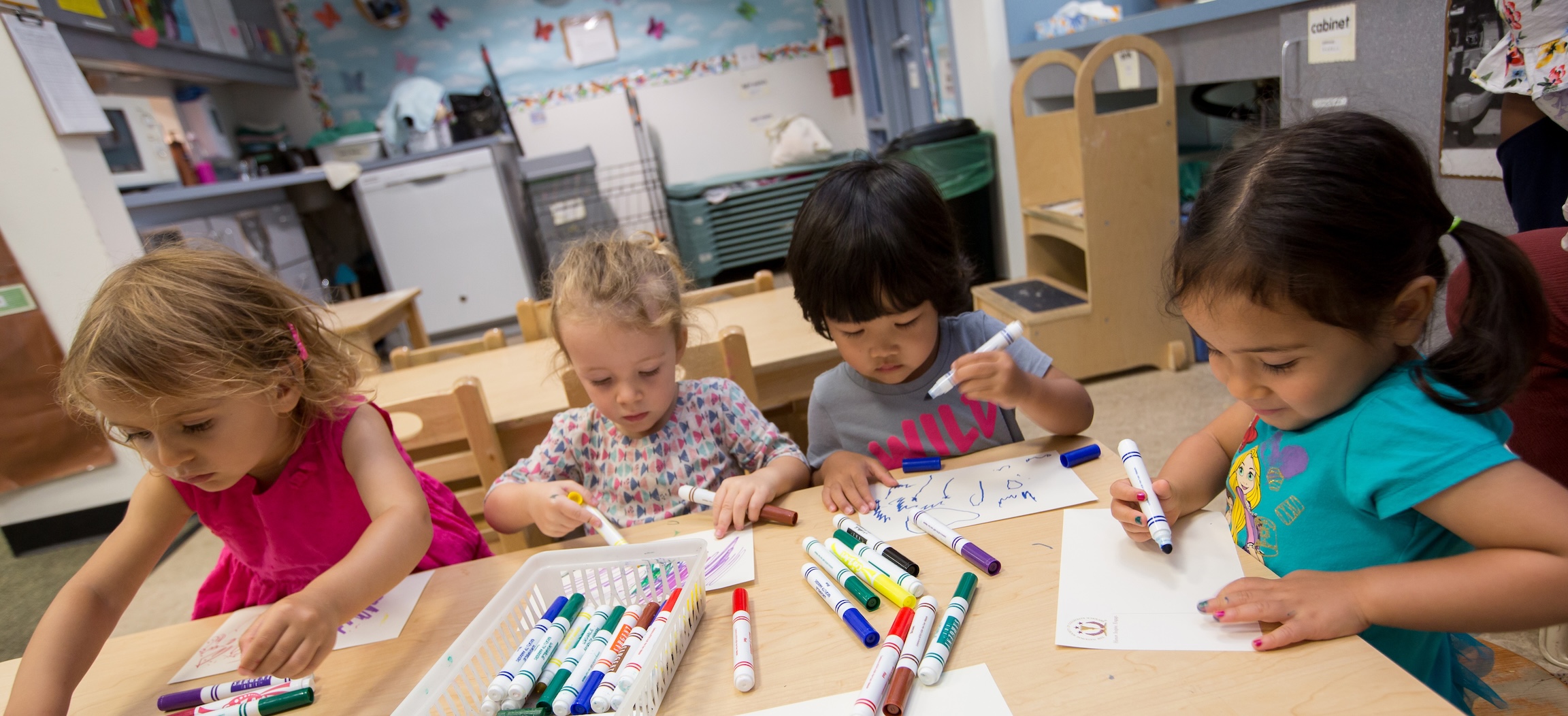 Four children draw and color at a desk at CECE.